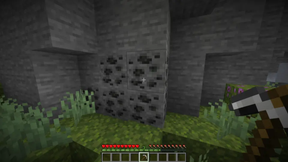 Joueur visant un filon de charbon dans une grotte Minecraft avec une pioche à la main